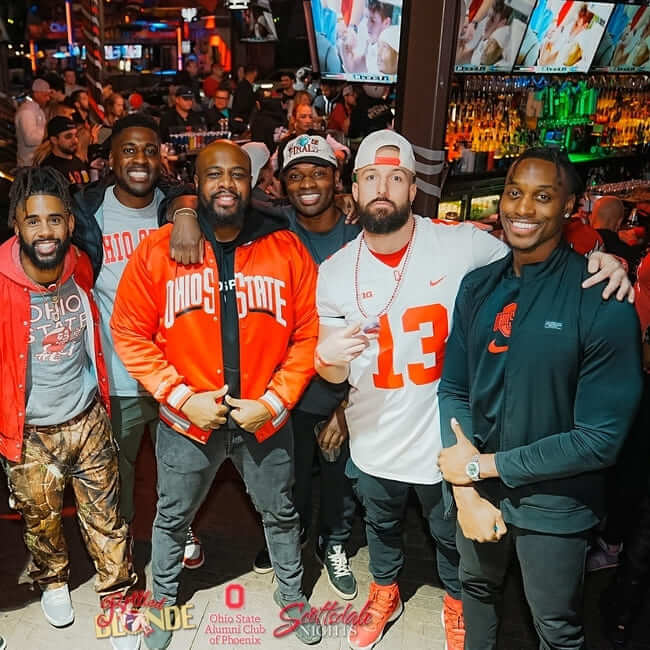 Group of friends in Ohio State gear posing at a crowded sports bar