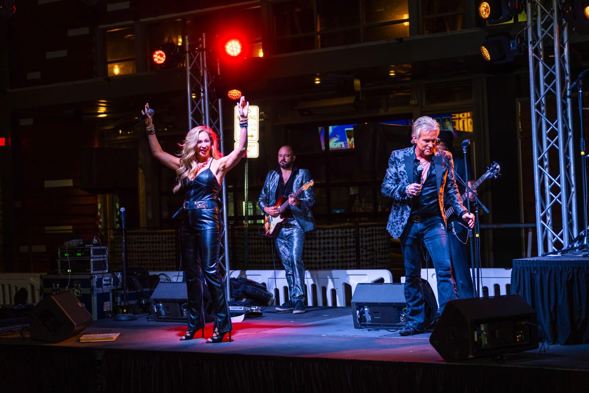 Live band performing on an outdoor stage at Bottled Blonde under colorful lights with a female singer and guitarists.