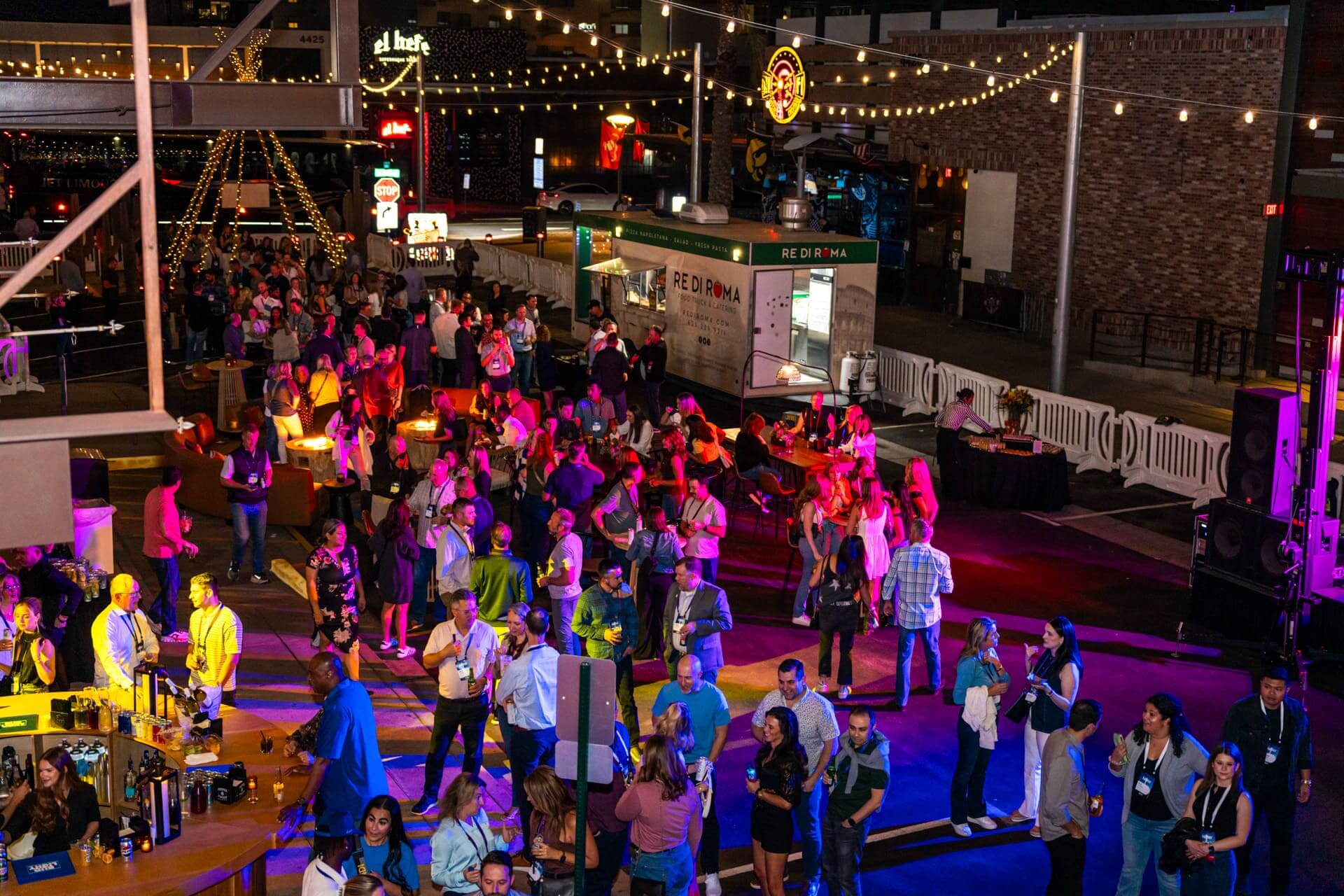 Vibrant crowd enjoying a nighttime outdoor event at Bottled Blonde, with string lights, vendor booths, and social areas.